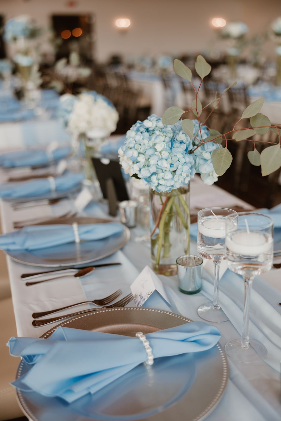 Elegant wedding reception table setting with light blue napkins and hydrangea centerpieces.