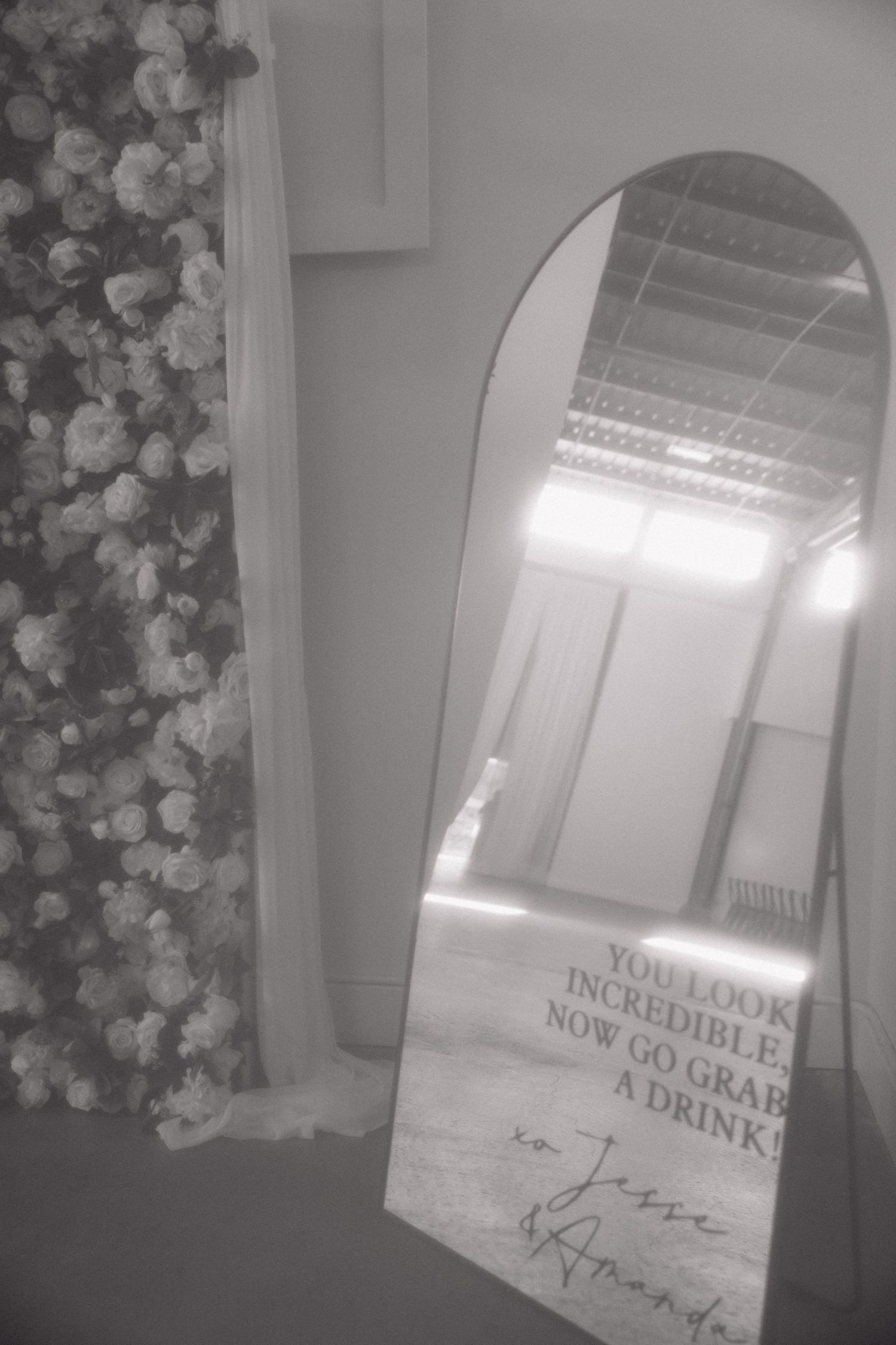 A black and white photograph of an arched mirror reflecting light and text with floral decorations visible to the side.