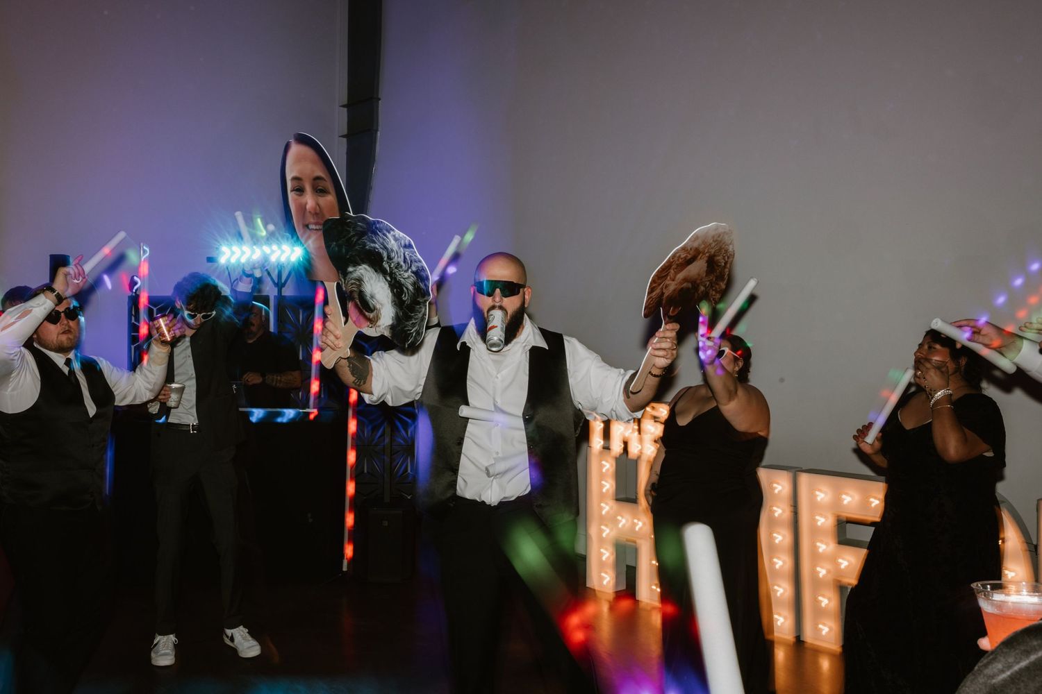 Wedding party dancing and celebrating with glow sticks in a dimly lit reception venue.