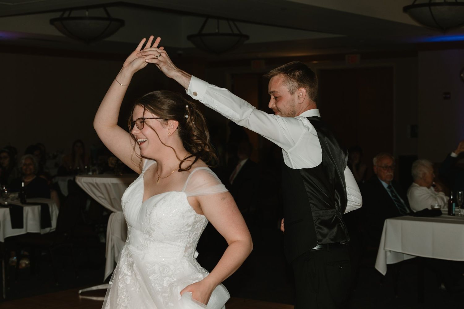 A couple dances together during their wedding celebration in a dimly lit reception hall.