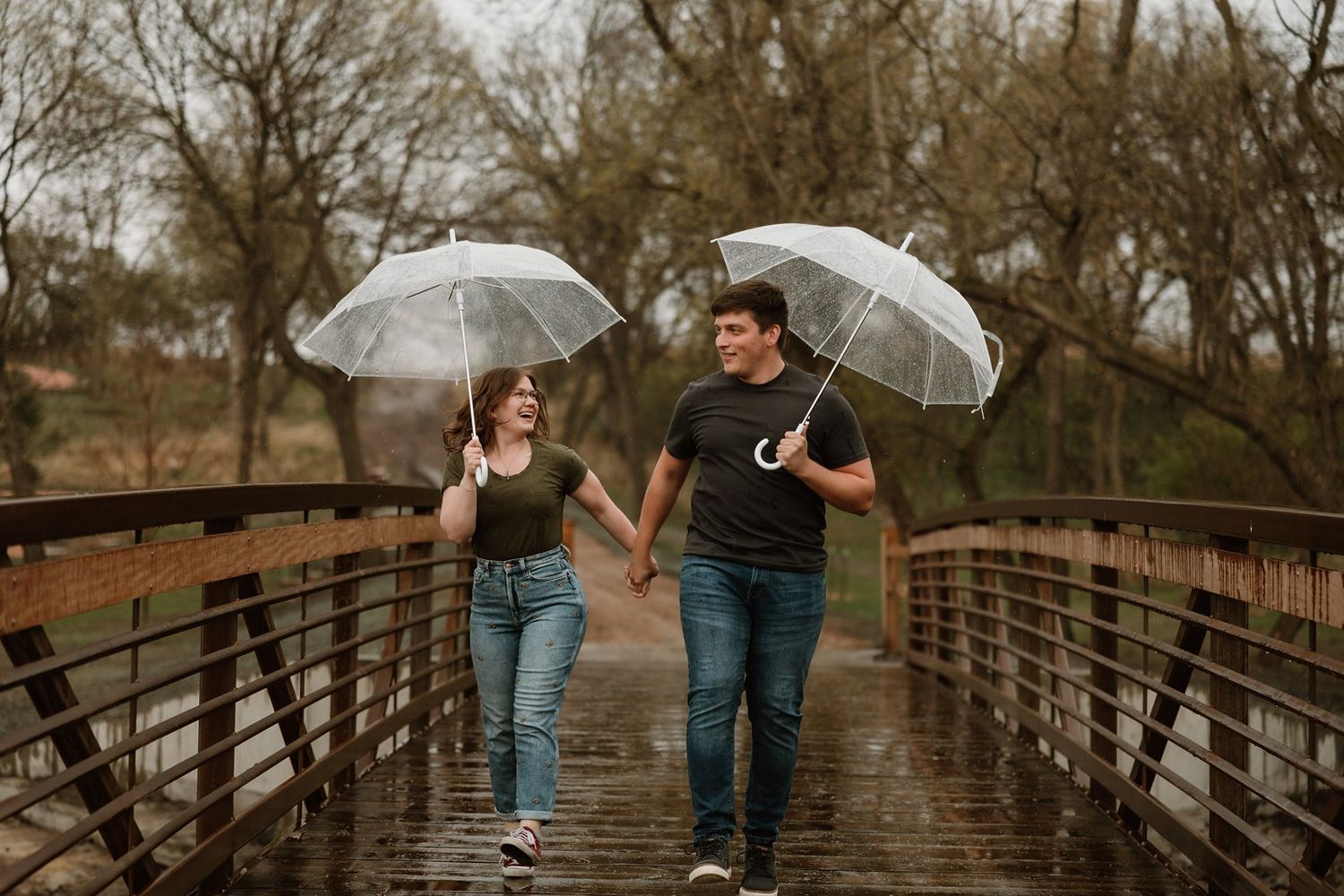 A couple with an umbrella walks across a wooden footbridge during a moody autumn day.