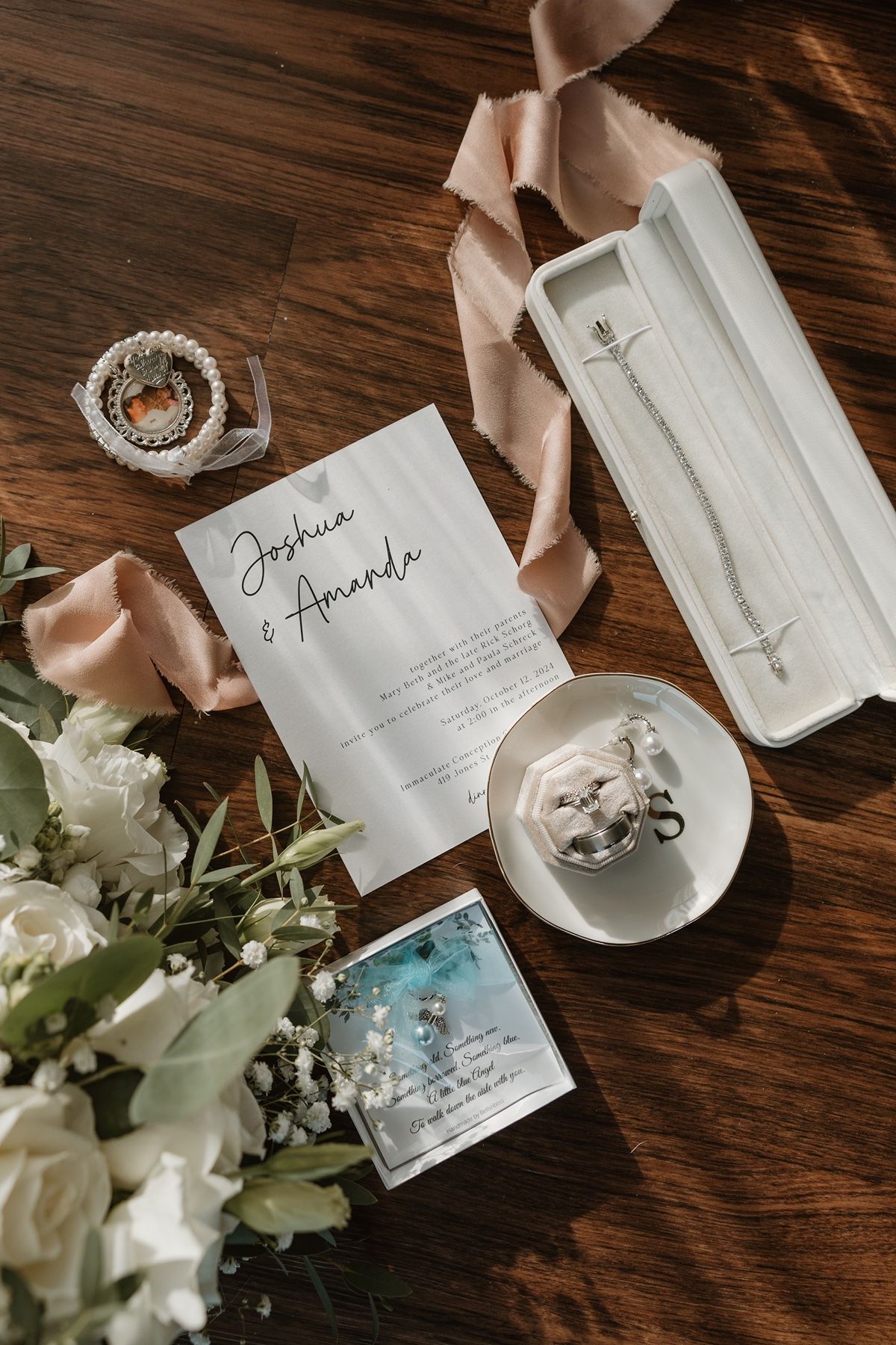 Elegant wedding flat lay with floral bouquet, invitation, jewelry, and ribbon on rustic wood table.