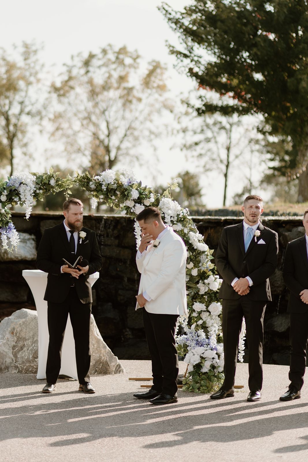 Wedding ceremony setup with floral arch and wedding party in formal attire.