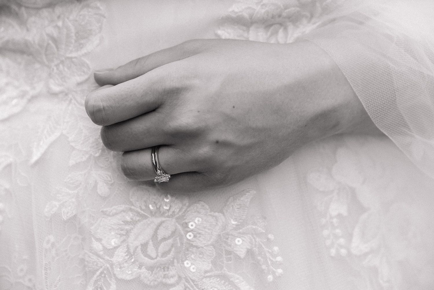 Close-up of hands showing off a sparkling diamond engagement ring against delicate white lace fabric.
