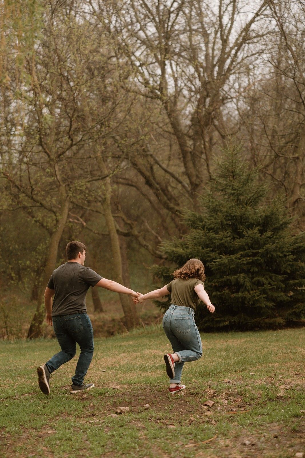 Playful couple balances and holds hands while leaning away from each other in a grassy park setting.