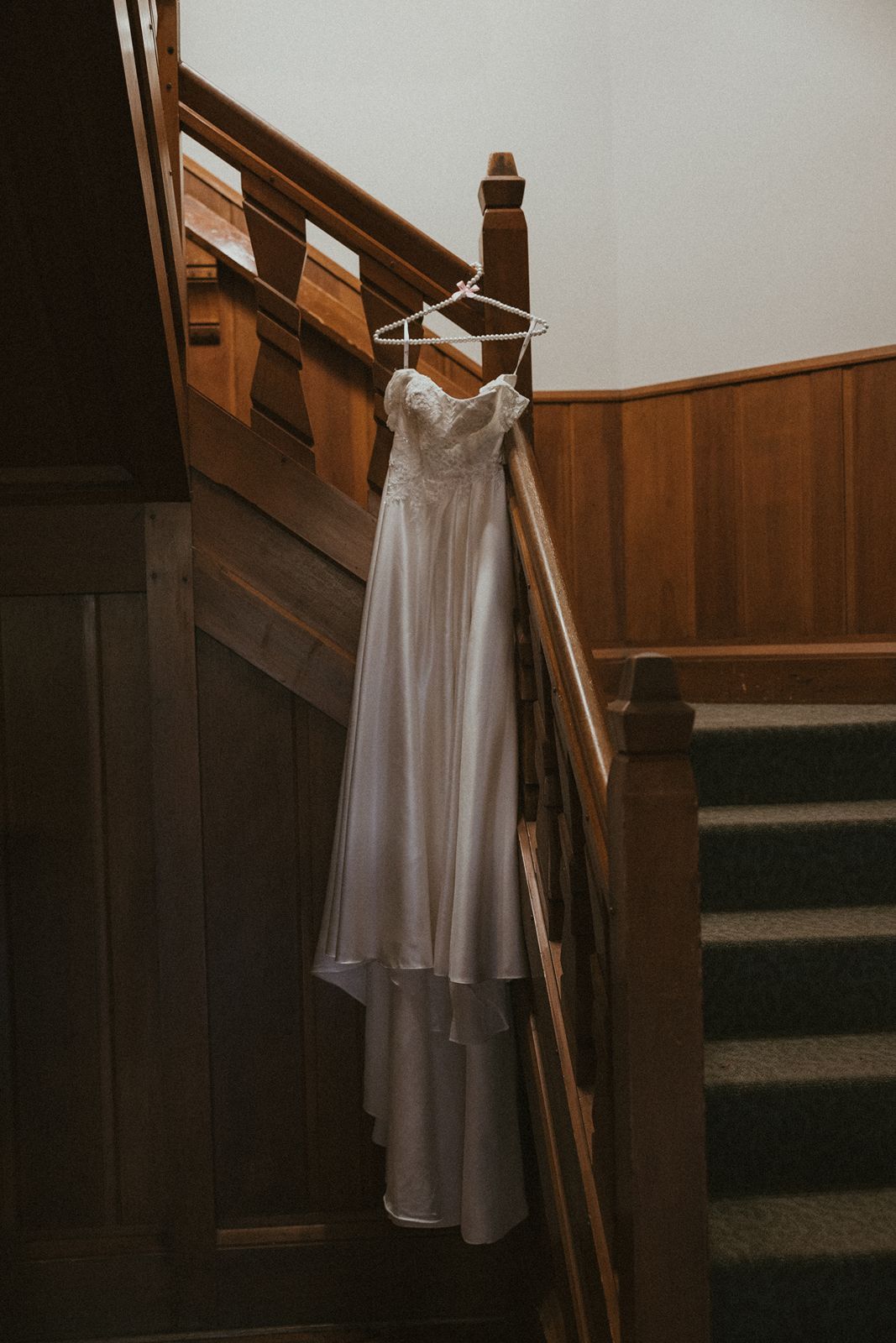 Elegant white wedding dress hanging on wooden staircase in dramatic lighting.