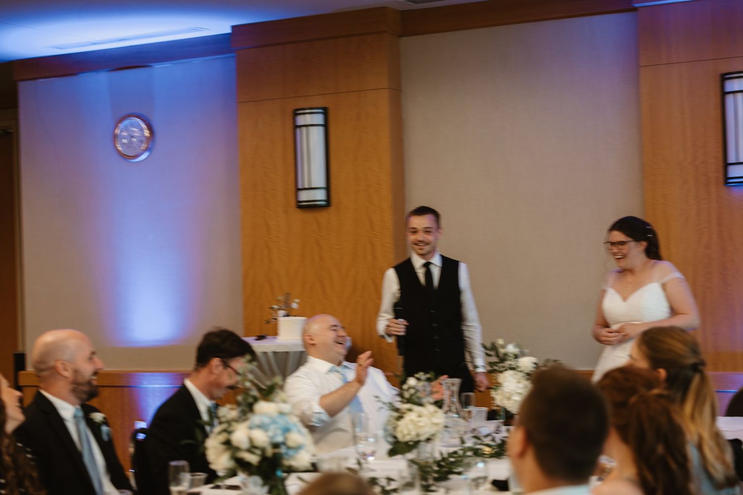 Wedding reception table scene with blue uplighting and formal dinner service during evening celebration at indoor venue.