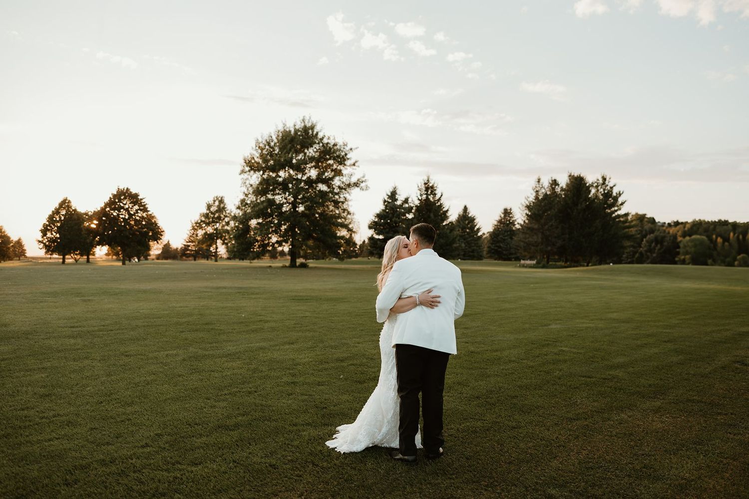 A silhouetted couple embraces on an expansive golf course during golden hour.