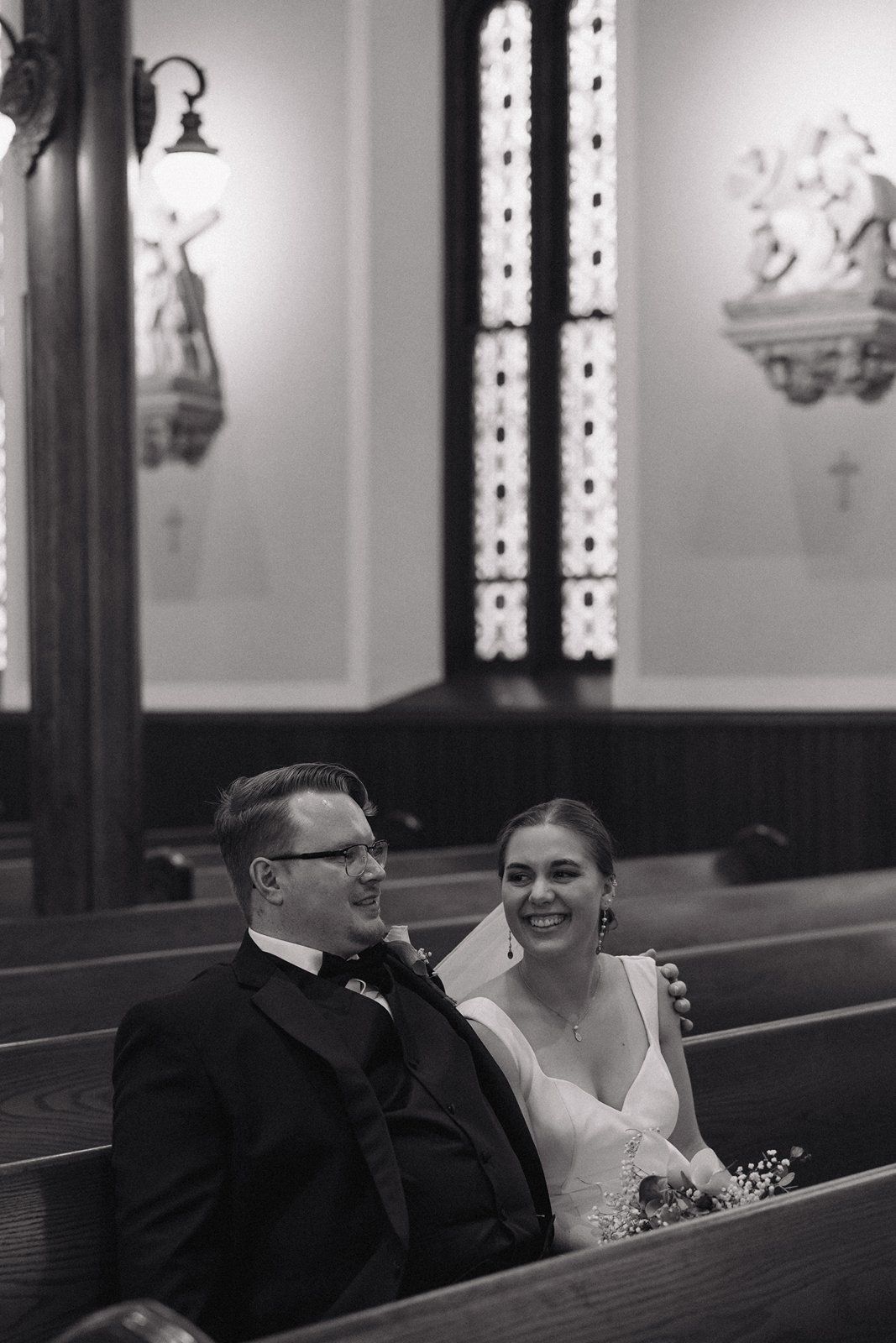 A black and white photograph of a couple sitting together in a church pew during their wedding ceremony.