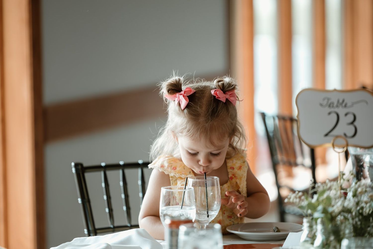 A small child sits at an elegant table setting with a glass of water and floral decorations.