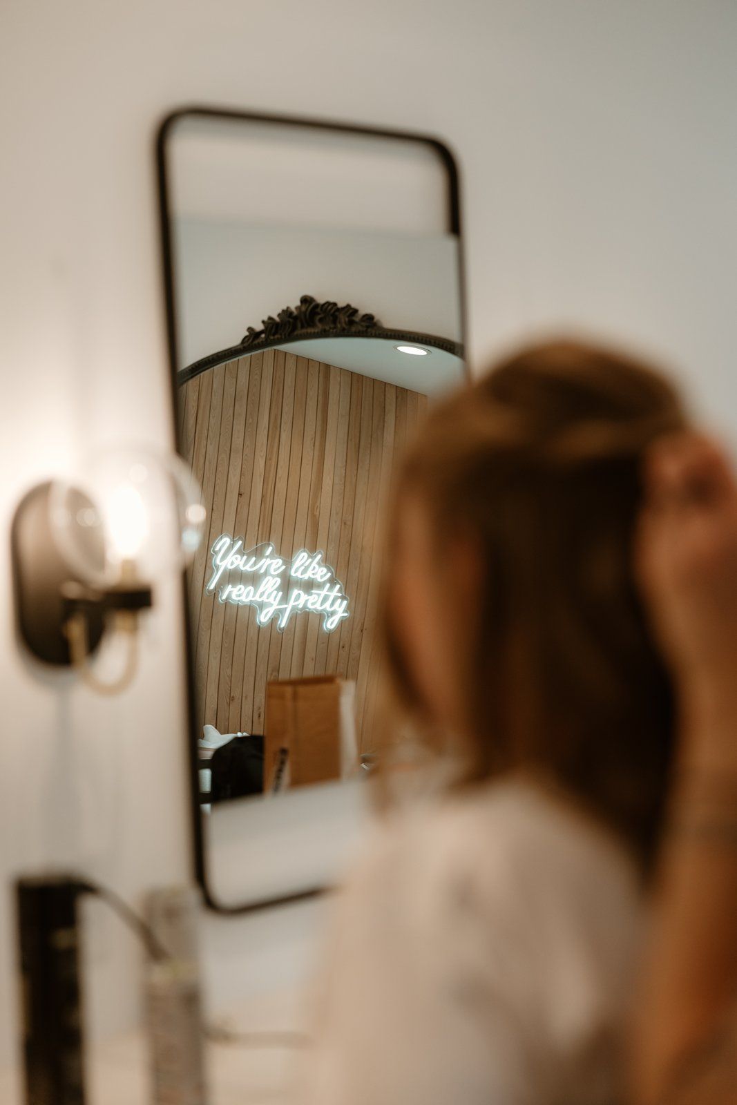 Blurred reflection in a bathroom mirror with neon text sign glowing in soft focus.