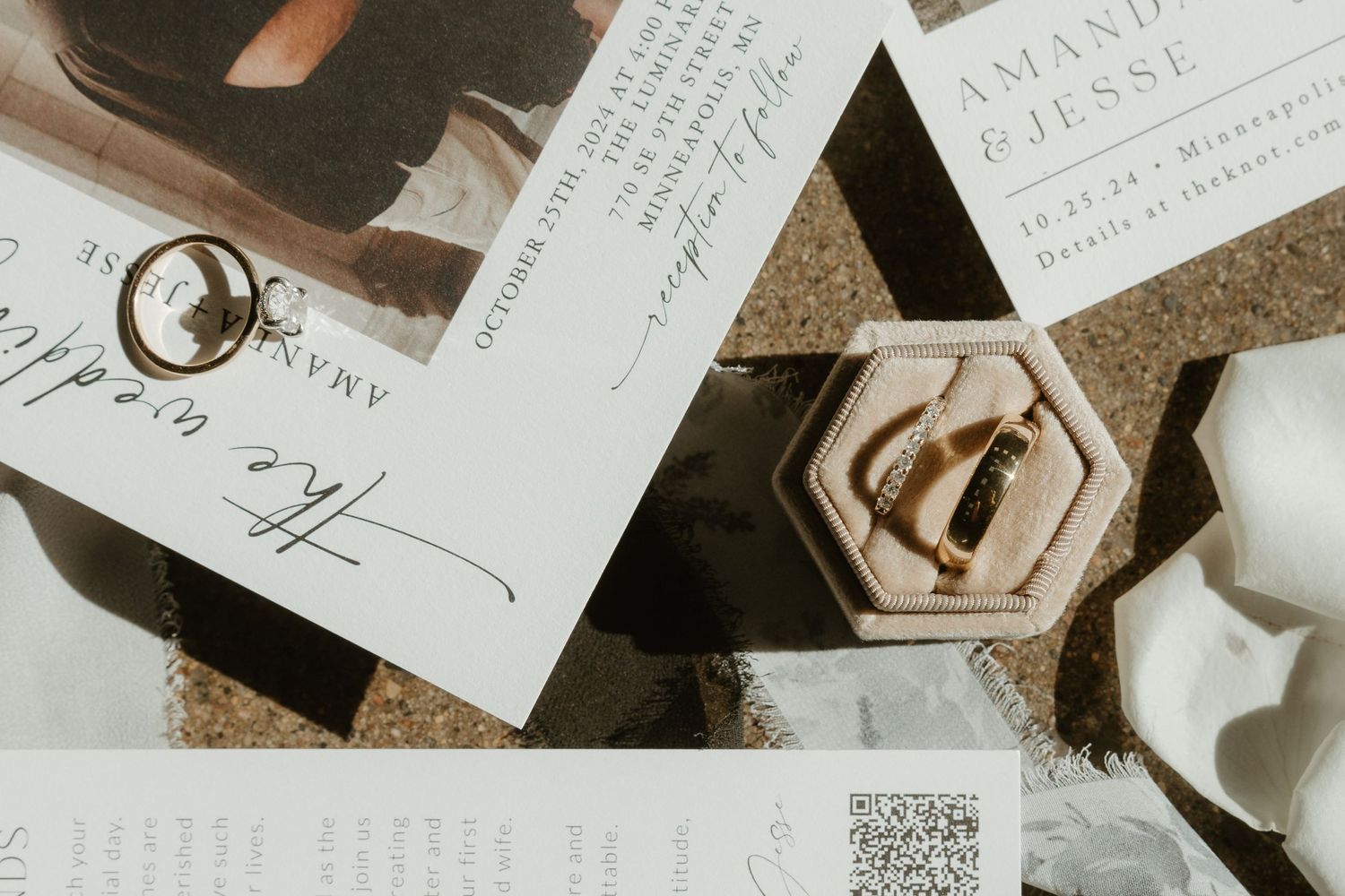 Wedding rings in a hexagonal box next to handwritten invitations and paper on a textured surface.