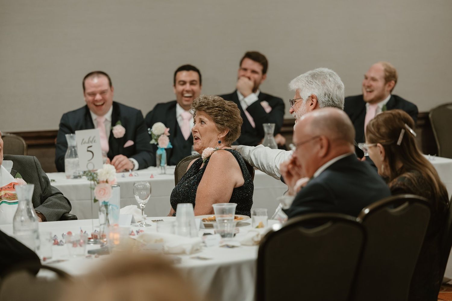 People seated at round tables during a formal dinner event share laughter and conversation in a banquet hall.