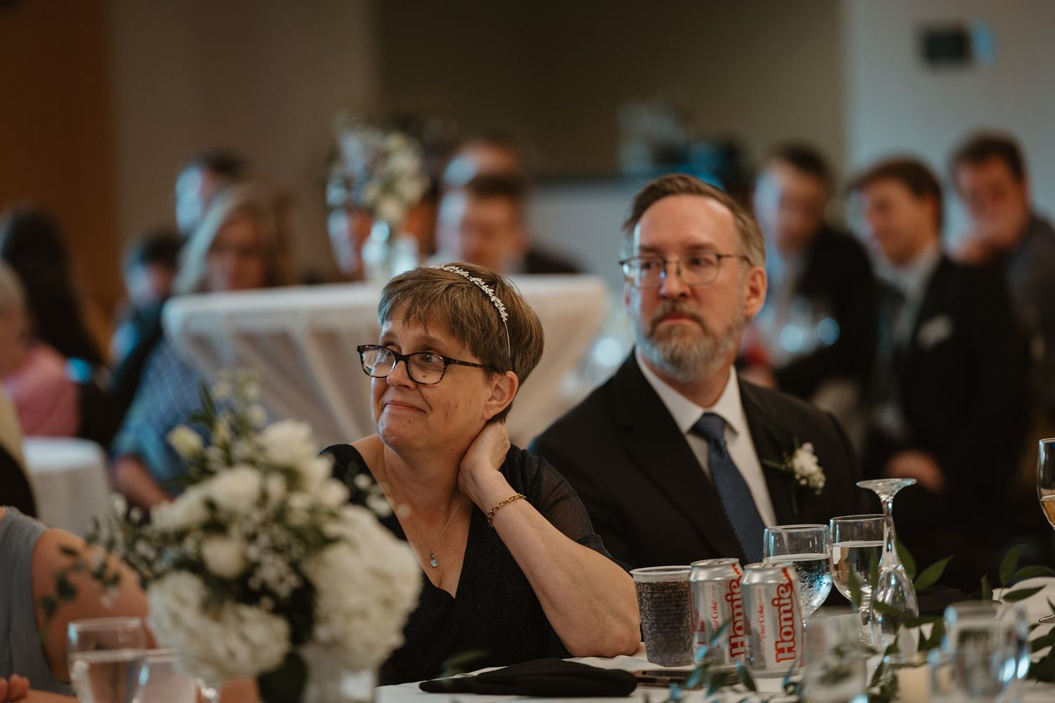 Guests seated at elegant wedding reception tables with white floral centerpieces and formal place settings.
