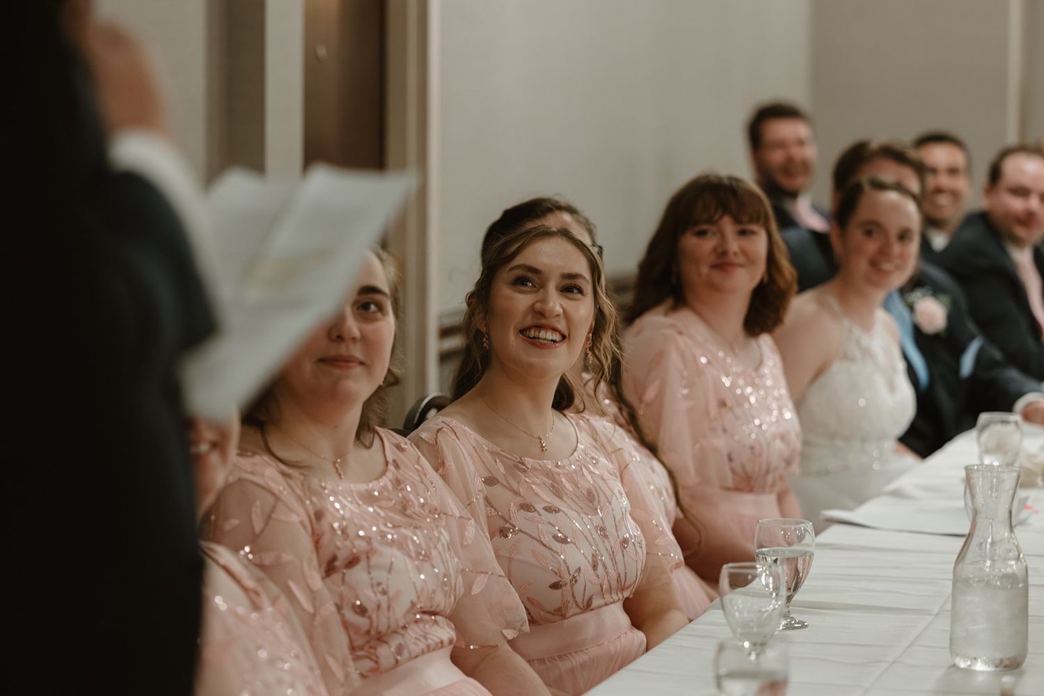 Wedding guests in pink bridesmaid dresses seated at long tables during a reception celebration.