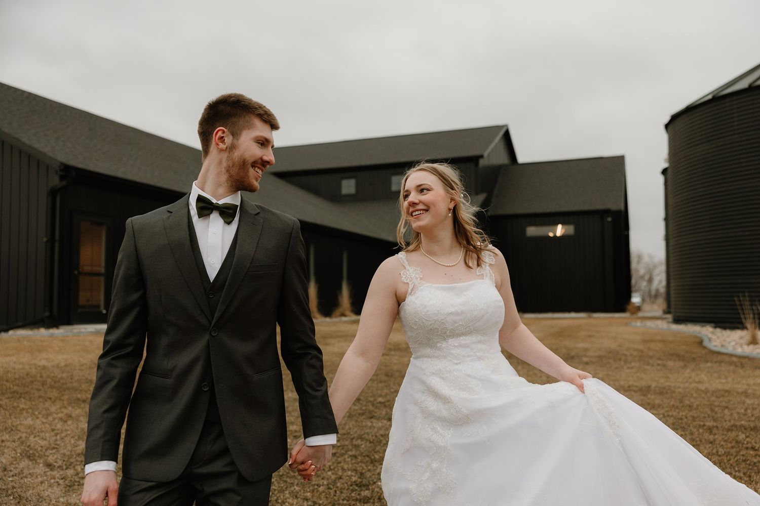 A bride and groom share a joyful moment together outside a modern black barn building on their wedding day.