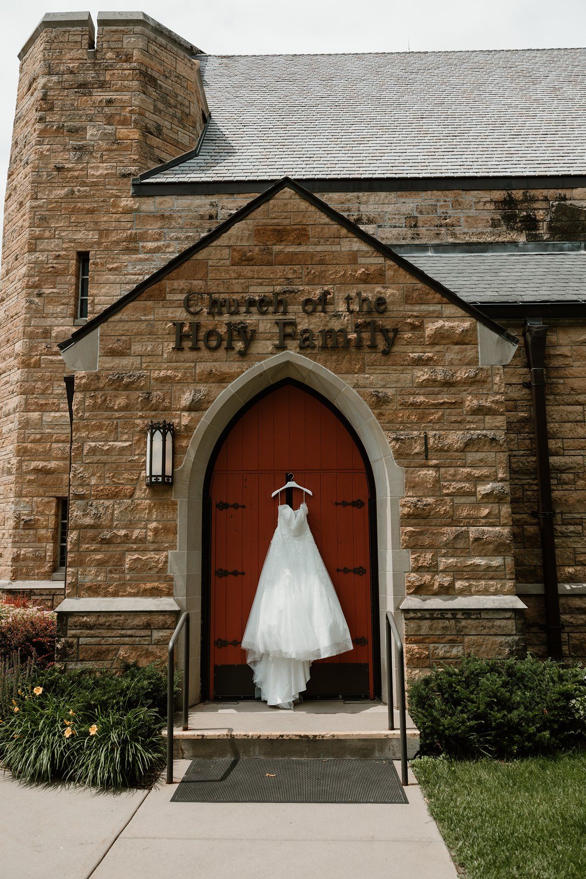 A white wedding dress hangs in the stone archway entrance of Church of the Holy Family.