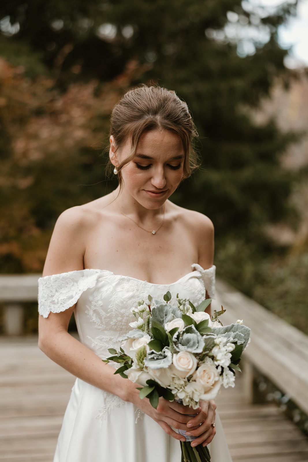Elegant bride holding white and green bouquet in classic off-shoulder wedding gown.
