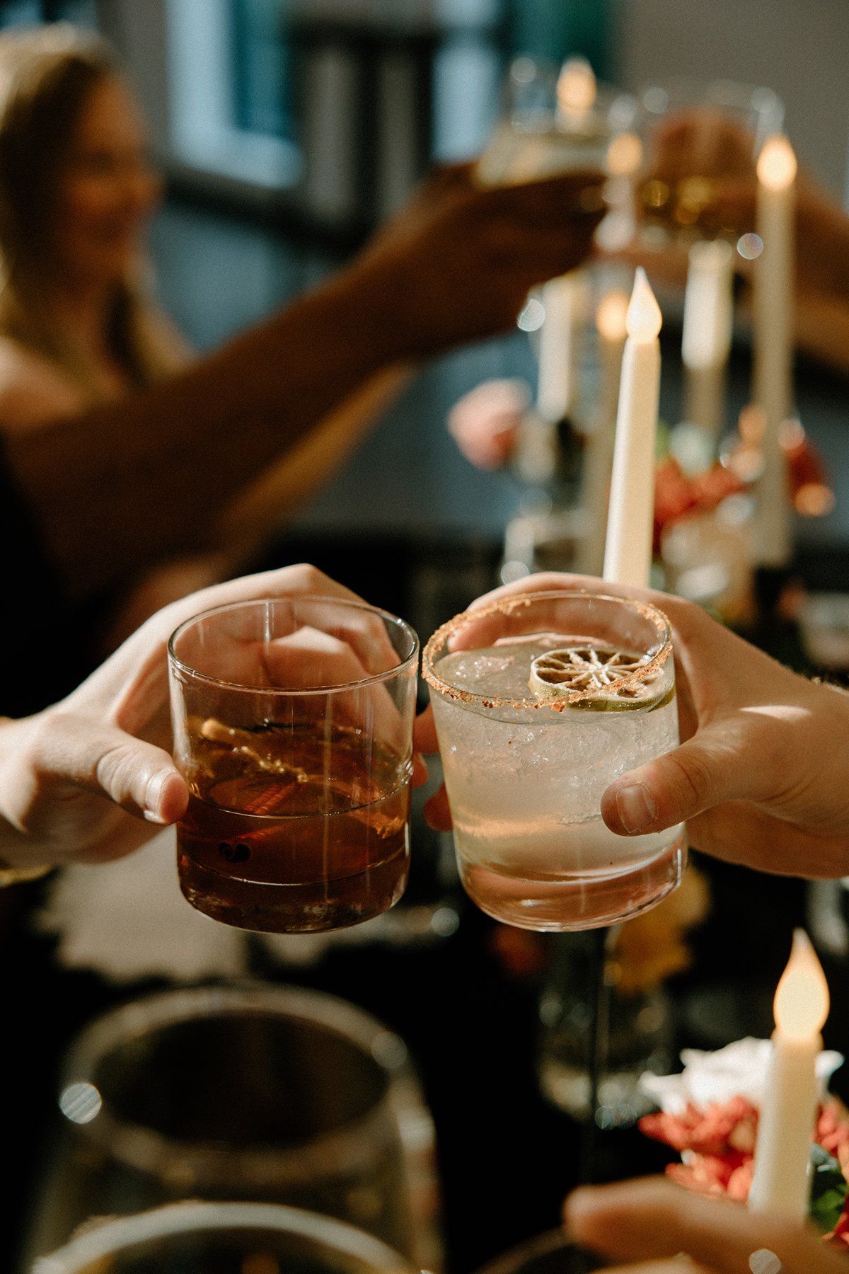 Friends clinking cocktail glasses in candlelight at an elegant wedding celebration.