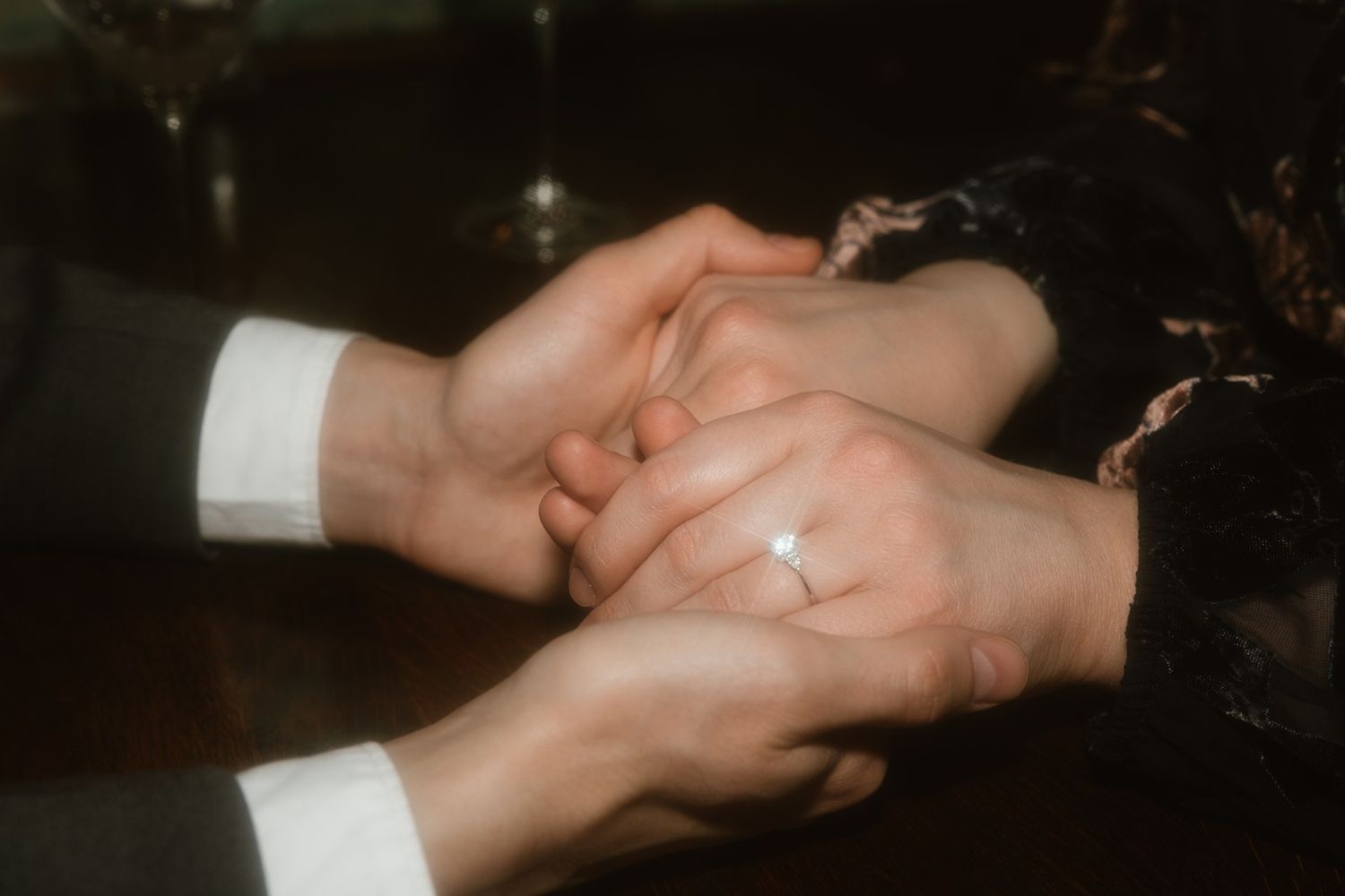 Close-up shot of hands holding each other with a sparkling diamond ring in romantic warm lighting.