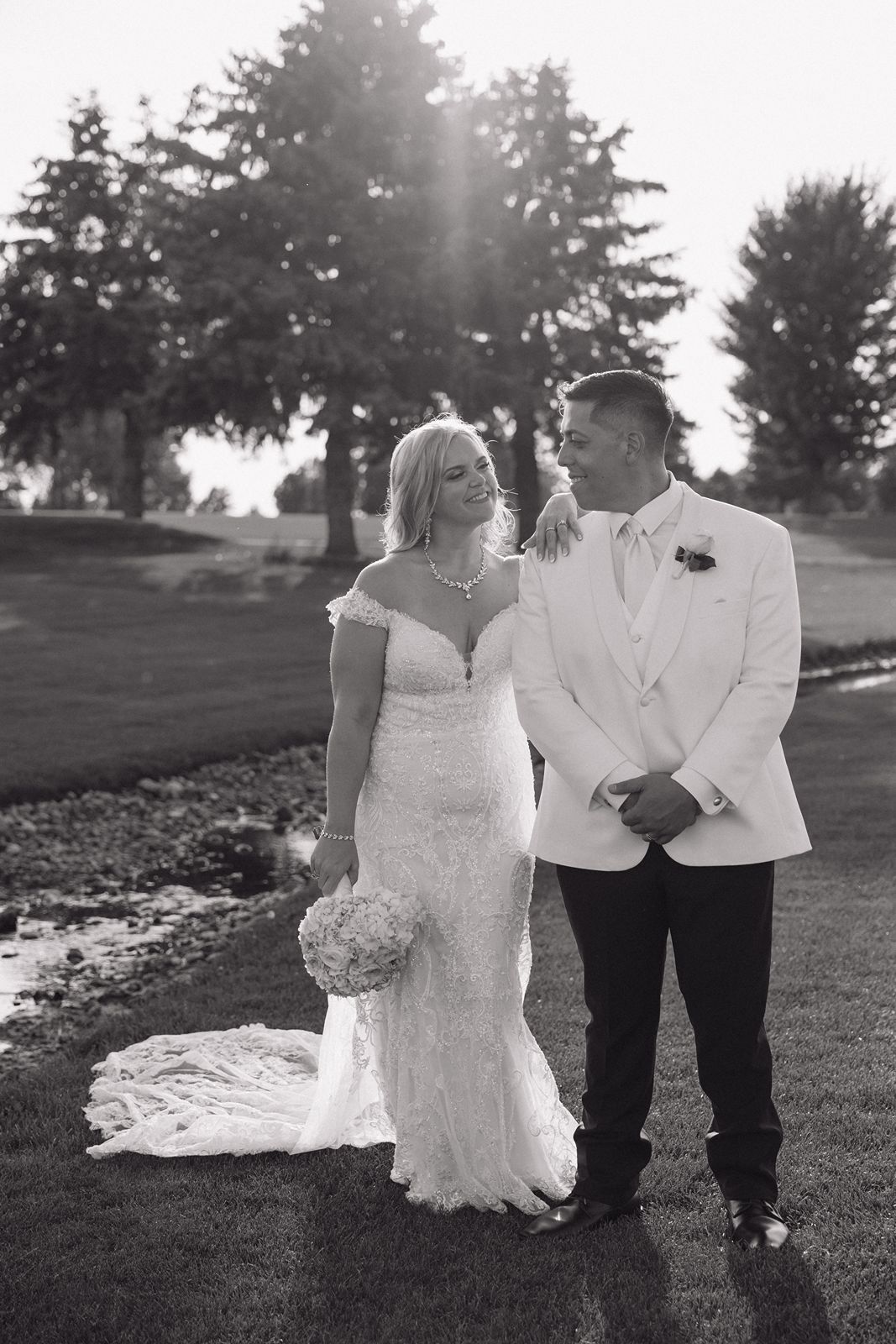 A black and white portrait of newlyweds standing together on a golf course.