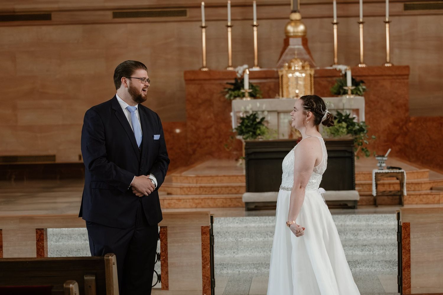 A romantic first look moment between newlyweds in a church with warm wooden walls and candlelit backdrop.