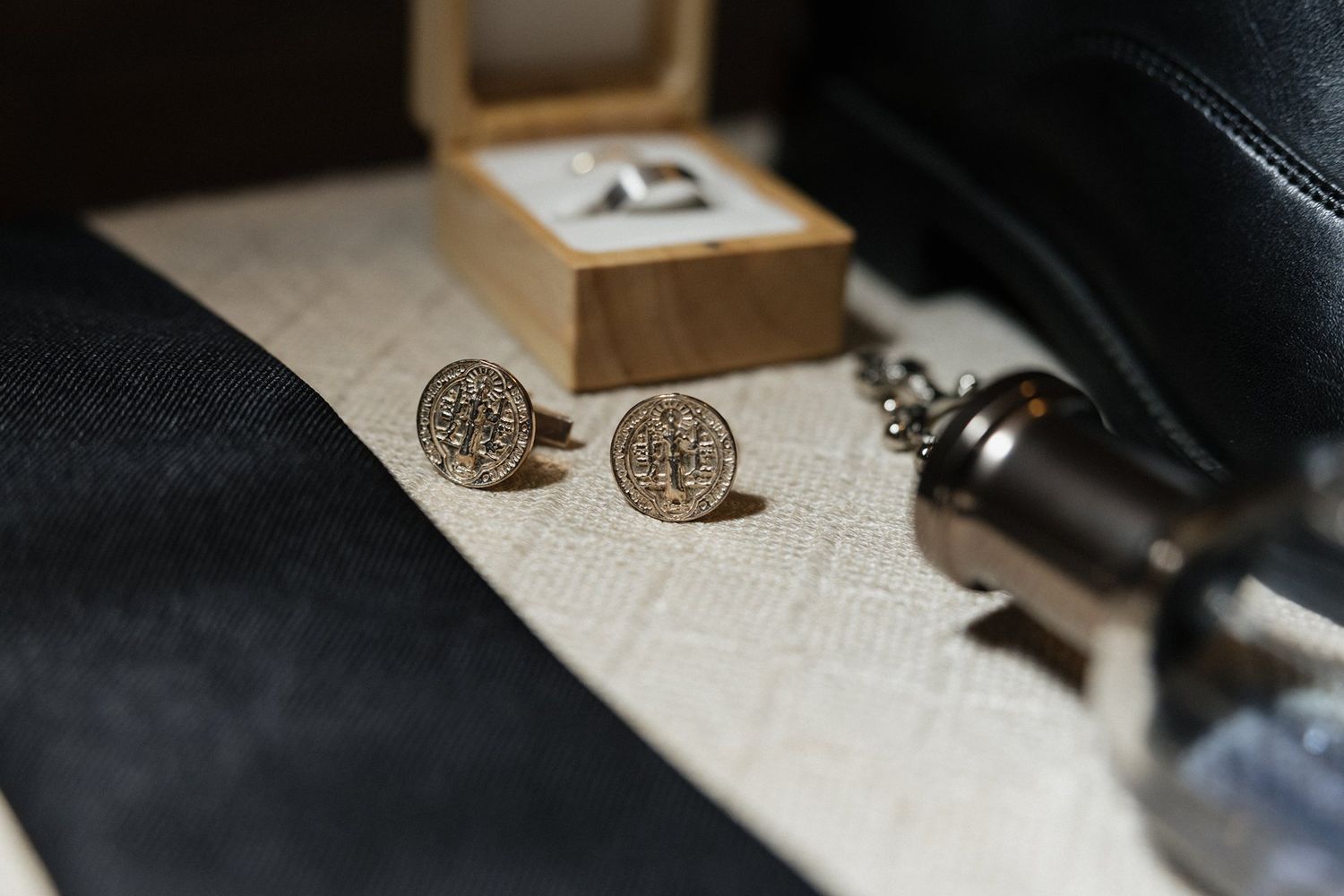 Elegant vintage-style metal cufflinks displayed on textured paper with a dark leather background and wooden box.