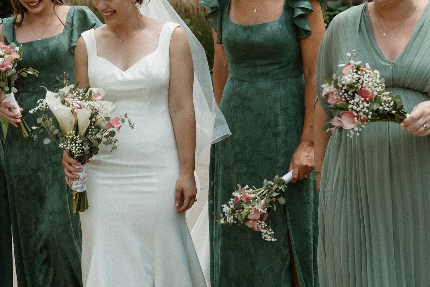 Close-up detail shot of bridesmaids holding floral bouquets while wearing different styles of sage green dresses.
