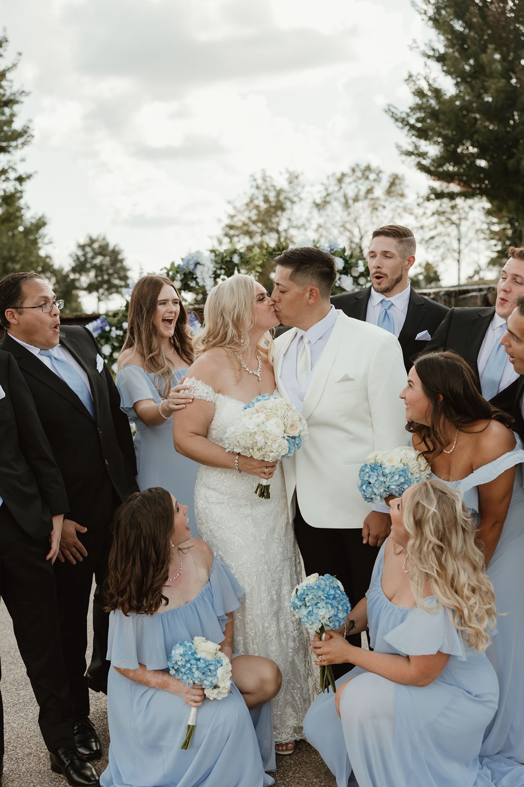 Wedding party gathered for photos with bridesmaids in light blue gowns holding bouquets.