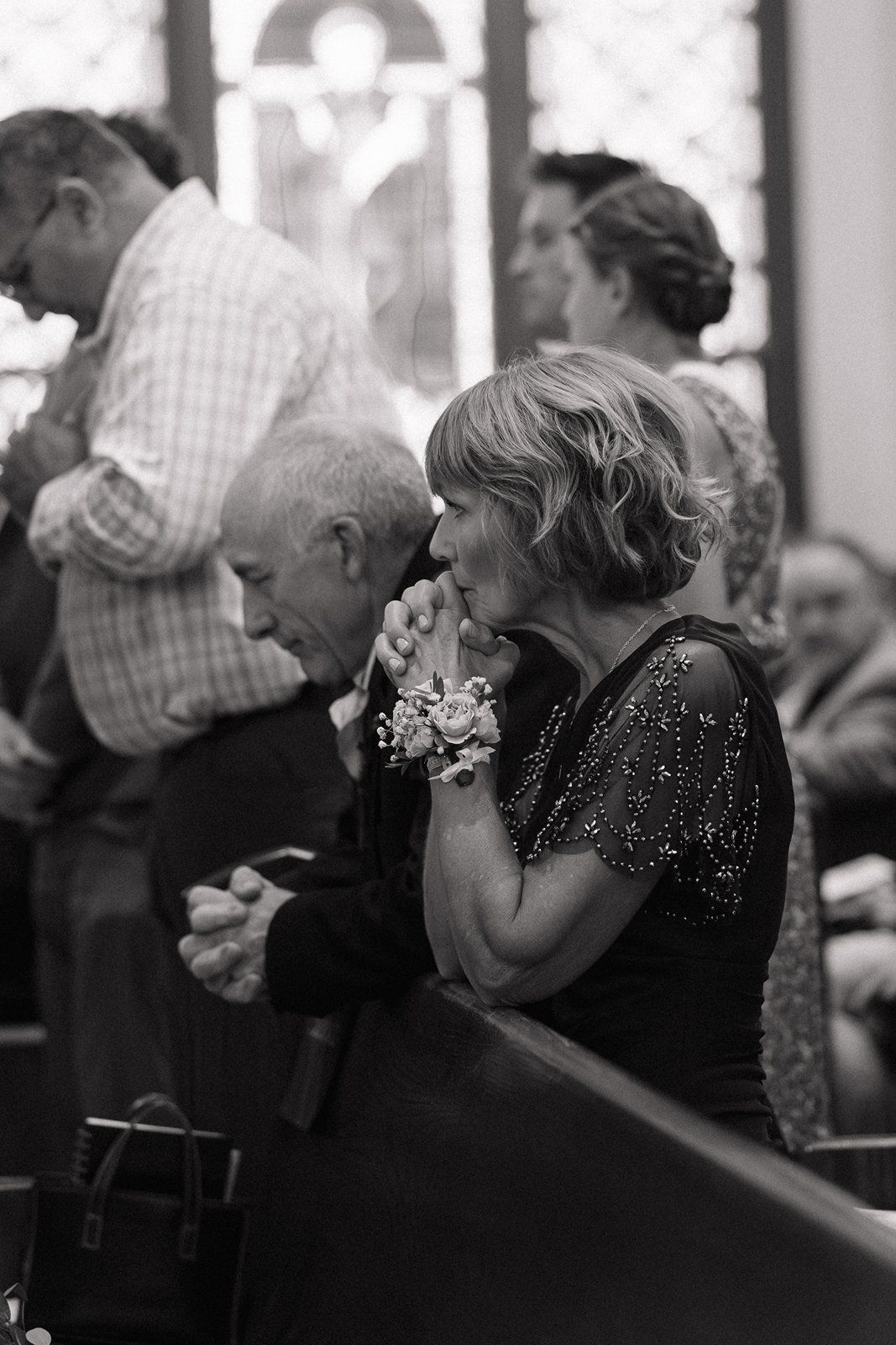 Wedding guests in formal attire seated in church pews during a ceremony.