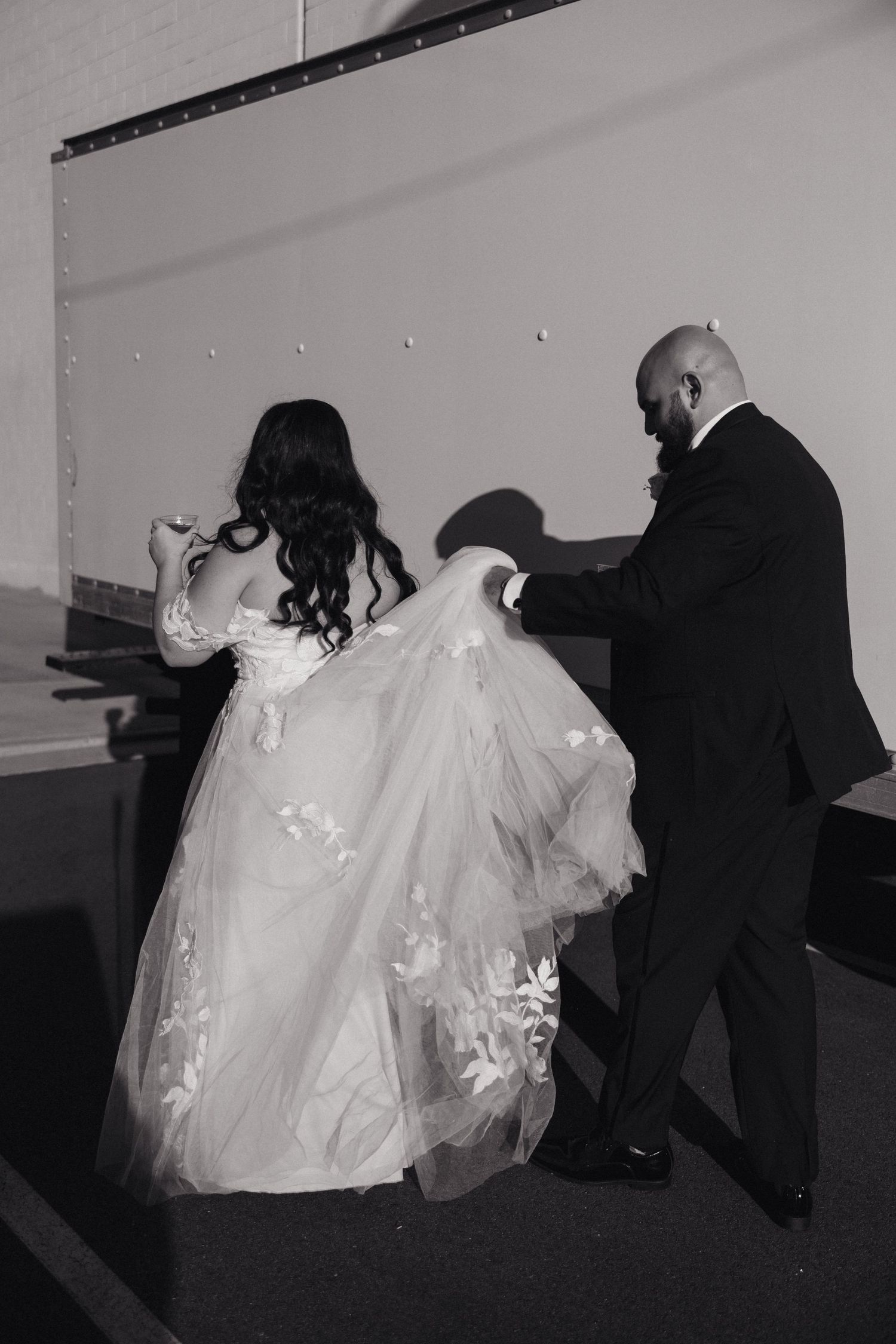 A black and white wedding photo captures the bride's dress being arranged before the ceremony.