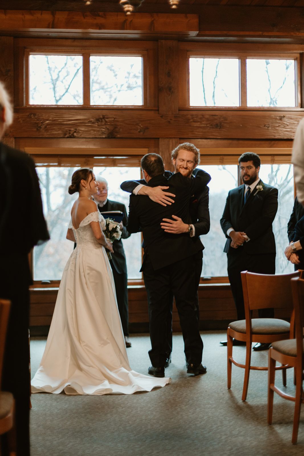 An emotional moment during a wedding ceremony in a rustic venue with large windows.