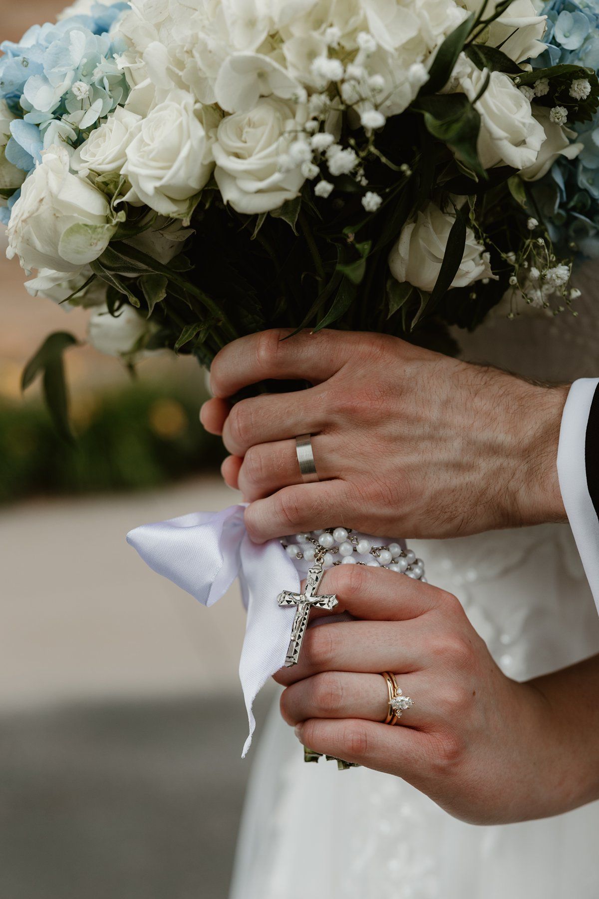 Close-up of elegant wedding rings and flower bouquet with white roses.