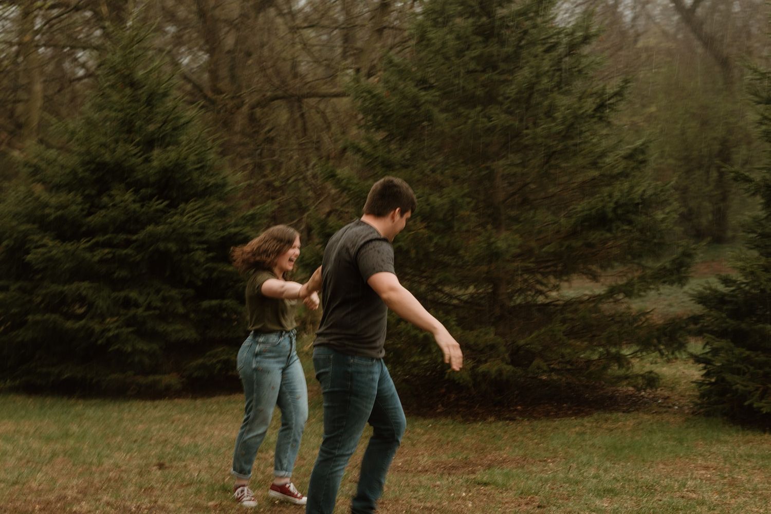 Two people engaged in a playful dance move outdoors with pine trees visible in the background.
