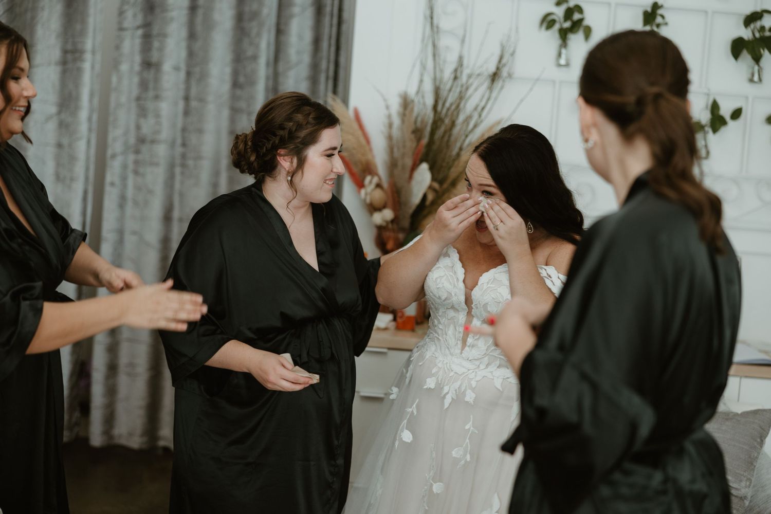 A wedding party getting ready in a room with bridesmaids in black robes and a bride in a white dress.