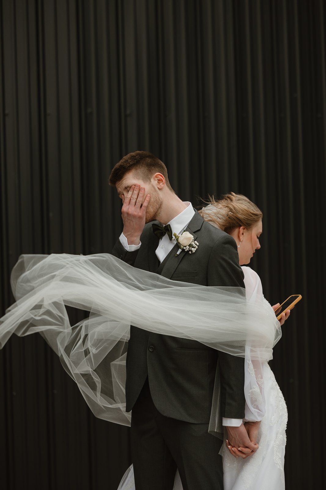 A bride and groom share an emotional moment during their first touch as her veil flows dramatically in the air.