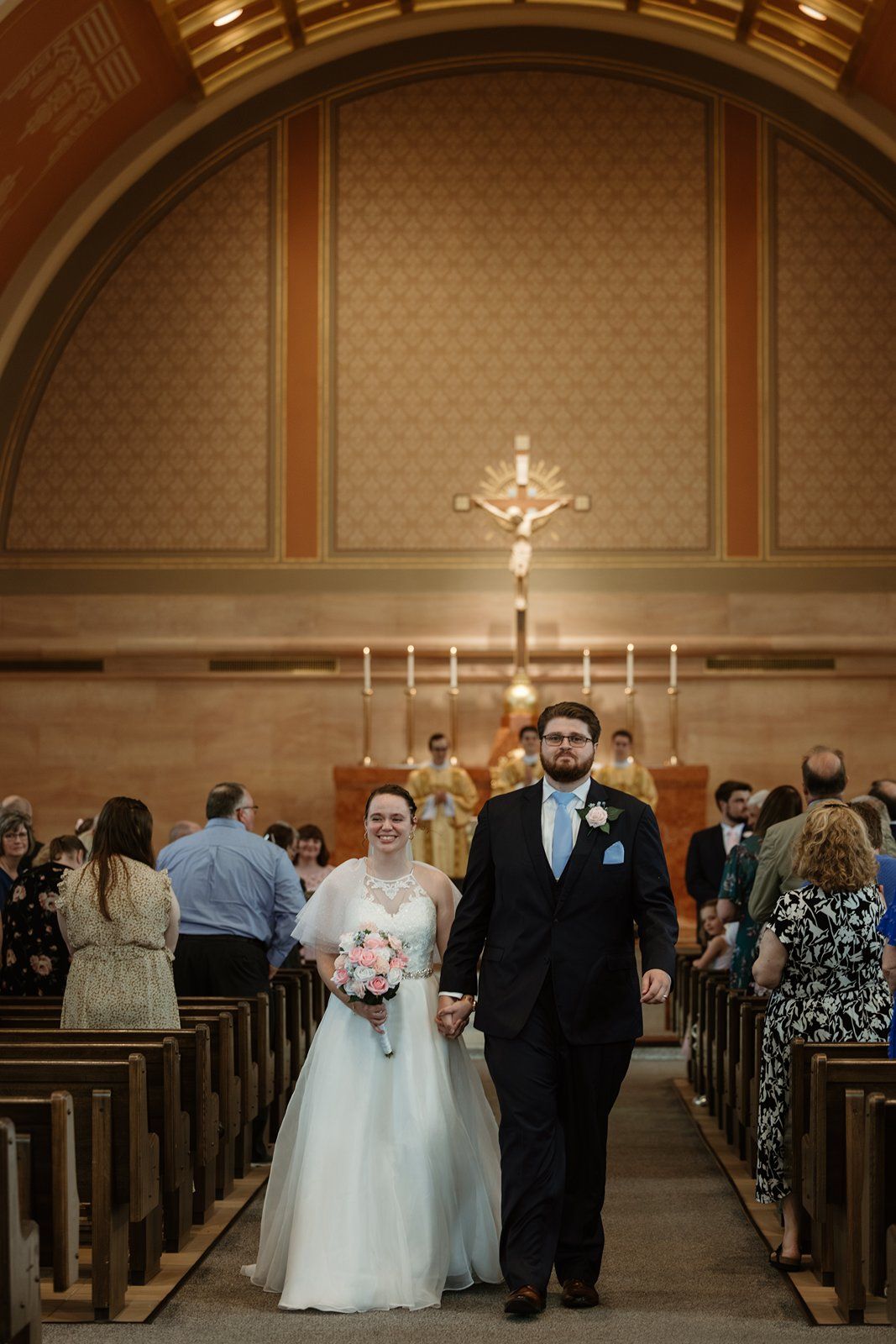 Church sanctuary with ornate ceiling, crucifix, and candelabras during a wedding ceremony.