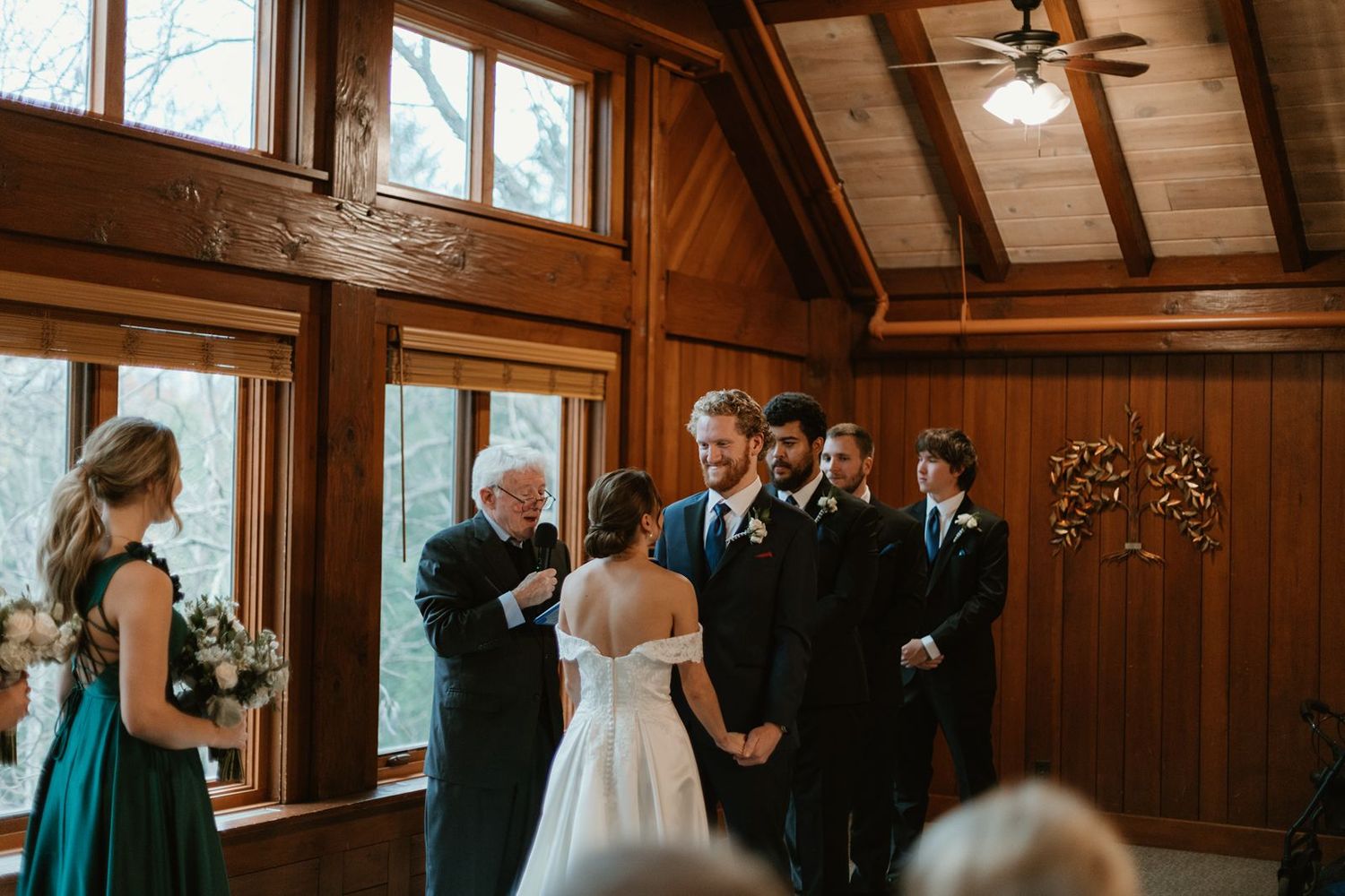 Wedding ceremony in progress inside a wooden chapel with natural light streaming through windows.