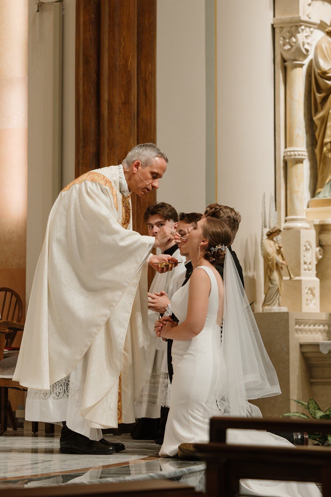 A religious ceremony takes place at the altar of an ornate Catholic church.