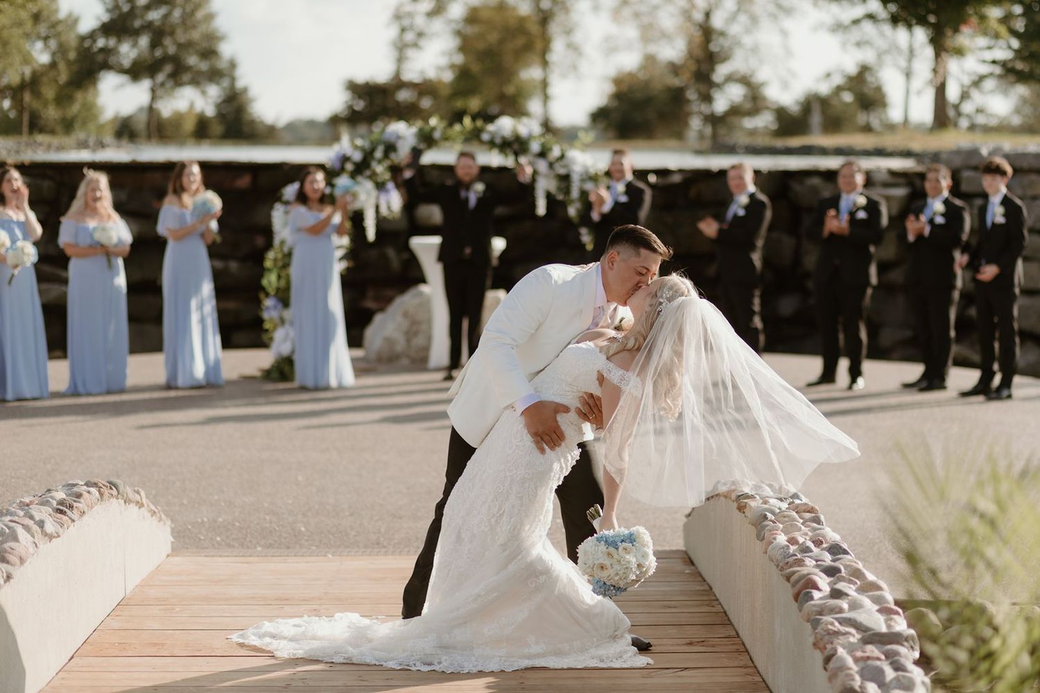 A dramatic wedding kiss captured during an outdoor ceremony with guests watching in the background.