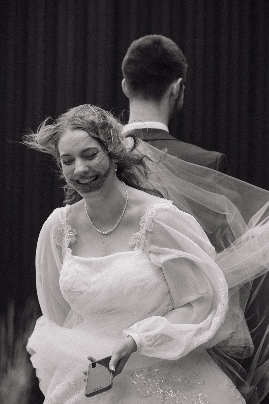 A bride in a flowing white wedding dress with a veil billowing dramatically in the wind.