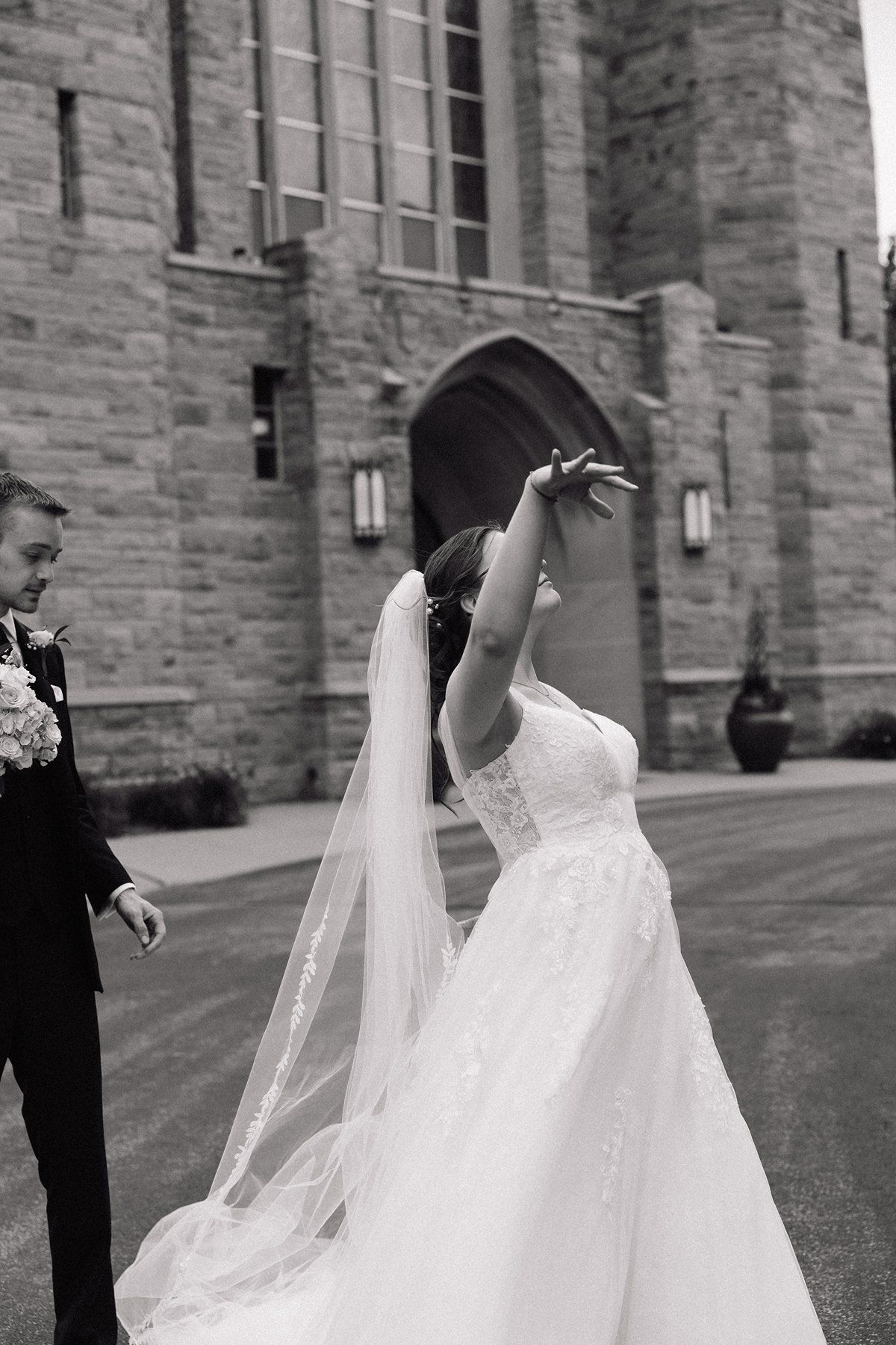 A romantic wedding couple spinning and dancing outside a stone church building.