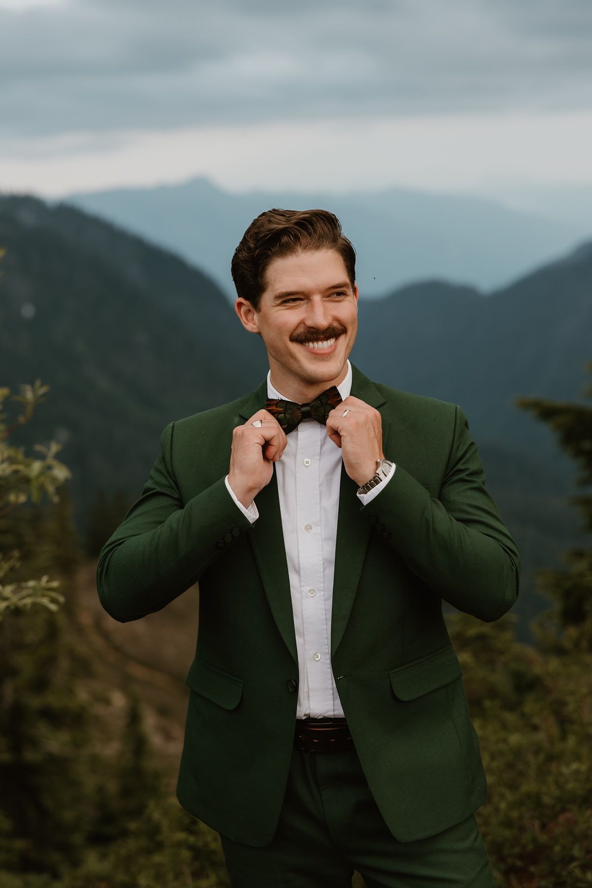 Groom adjusts tie during his adventure elopement in the mountains.