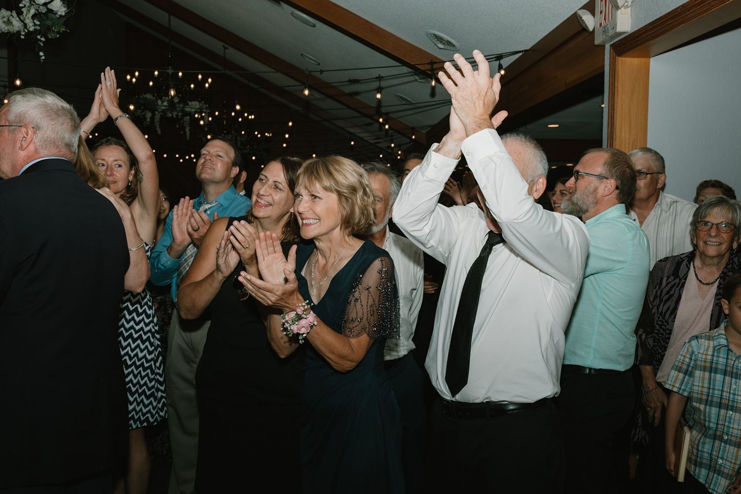 Wedding guests clap and raise their hands while dancing and celebrating on the dance floor.
