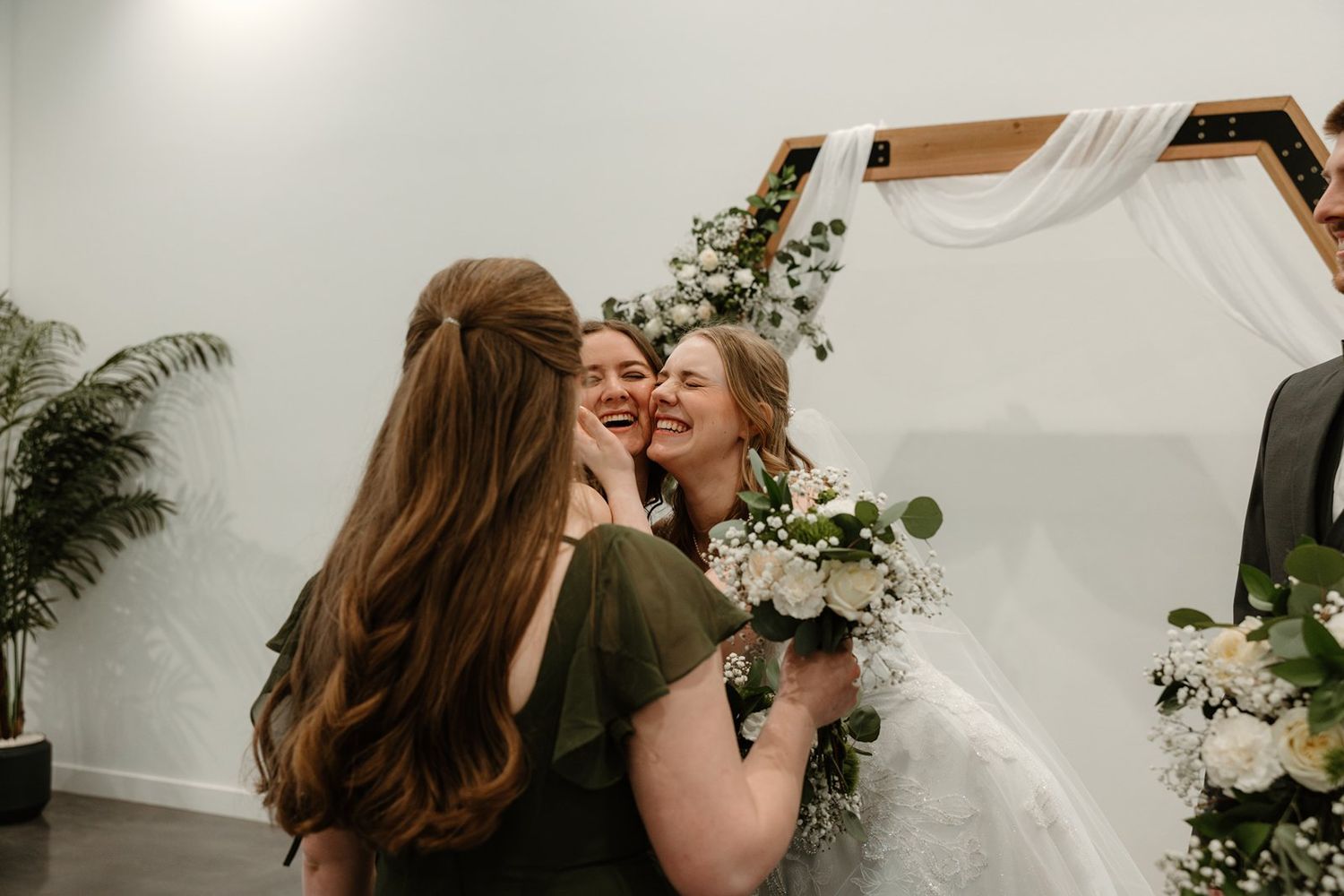 A romantic couple shares an intimate kiss in a rustic wedding venue decorated with greenery and white flowers.