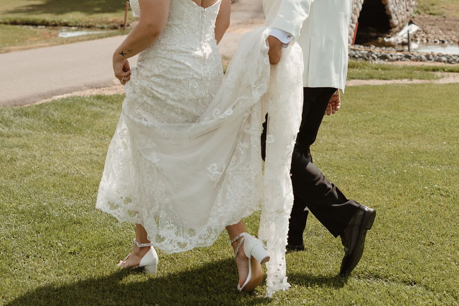 Close-up shot of wedding attire details as couple walks on grass path.
