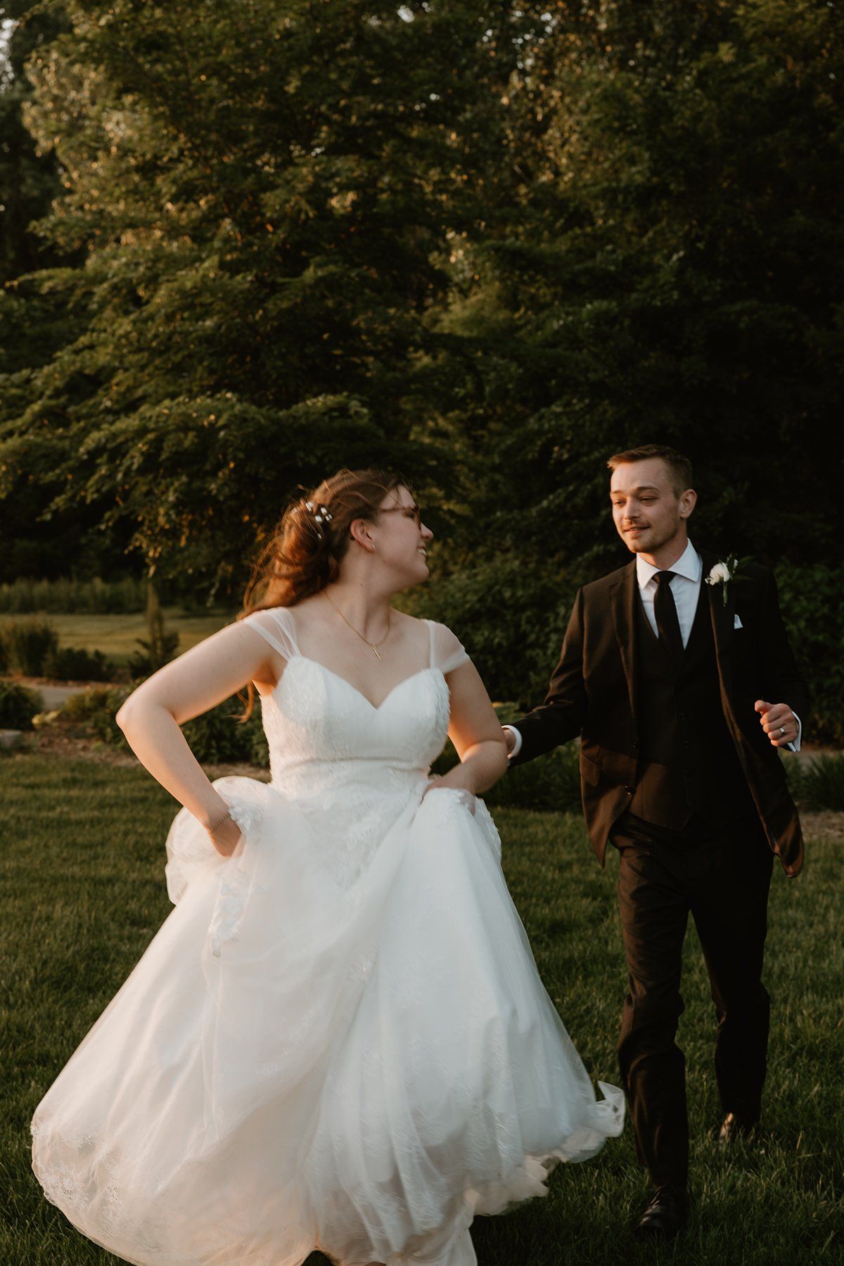 A romantic wedding photo taken at sunset showing a couple in formal attire dancing on a lush green lawn.