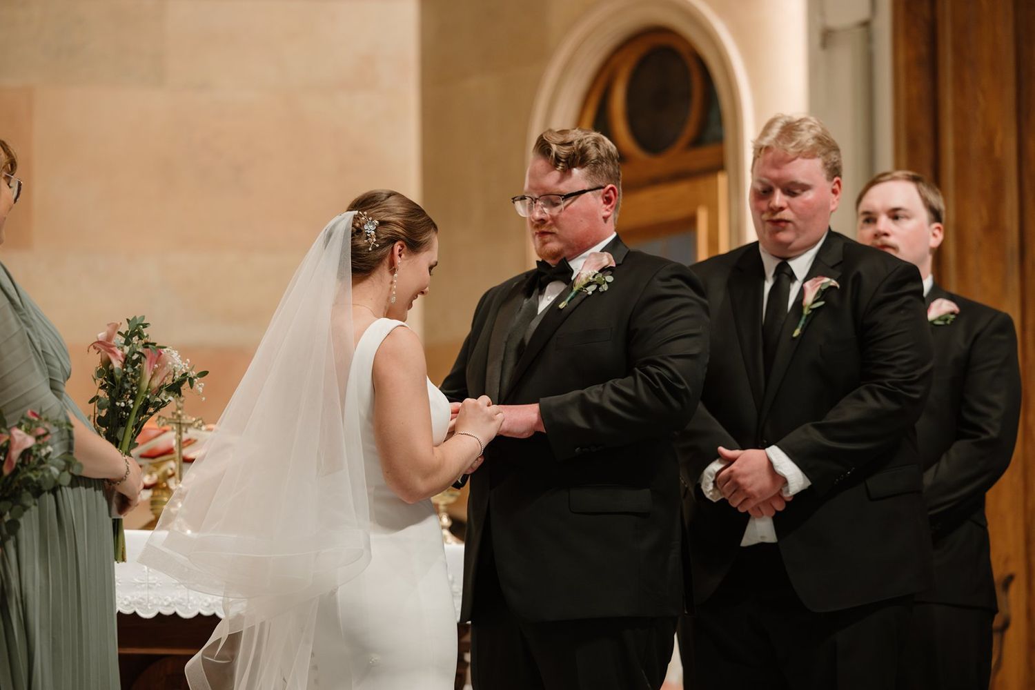 Wedding ceremony participants exchanging vows at the altar in an elegant church setting.