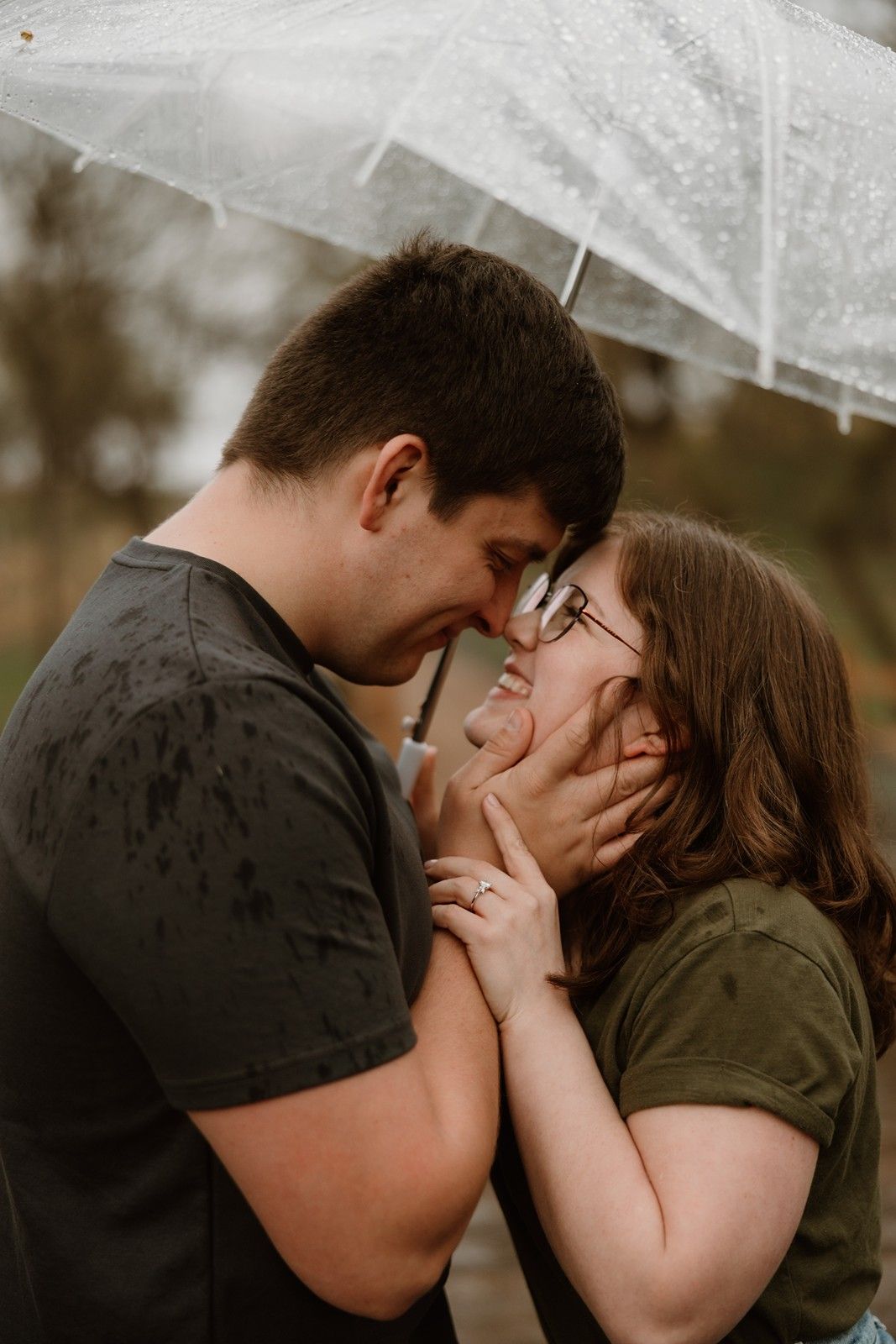 Two people share a romantic moment under a white umbrella in a rainy outdoor setting with bokeh background effect.