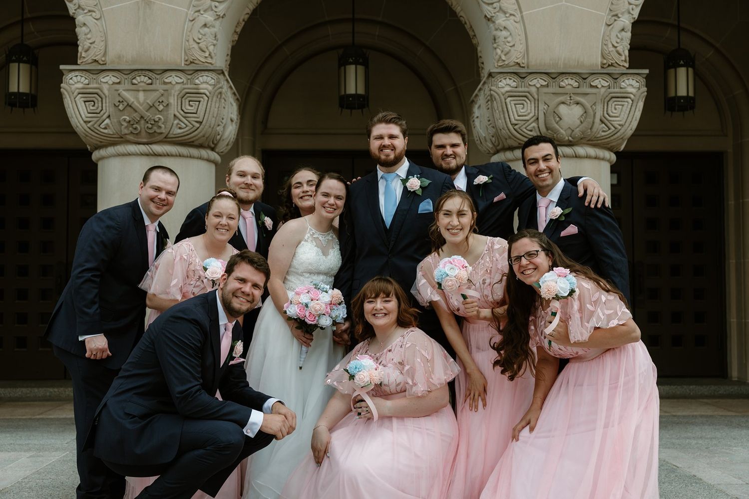 Wedding party poses together on stone steps in coordinated pink and navy blue formal attire.